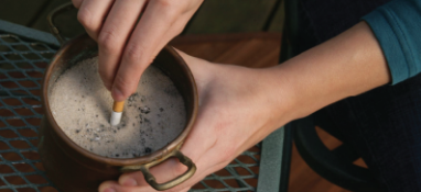 Two hands putting out a cigarette butt in sand